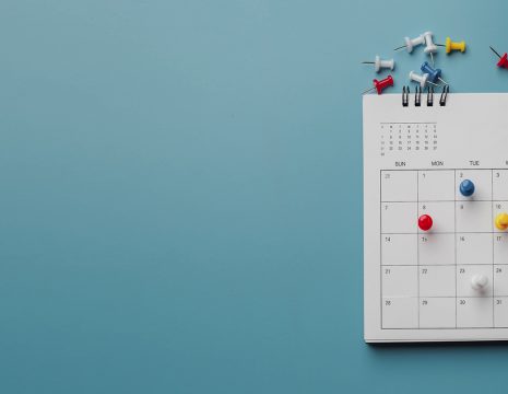 Dull blue background. CPD calendar with colourful pins placed on different dates.